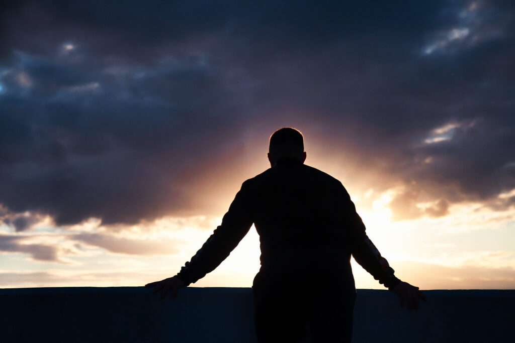 Silueta de un hombre parado al aire libre frente a un . Light rays burst from behind him.